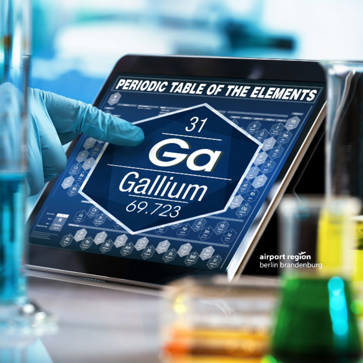 Picture shows a human hand in a laboratory environment pointing at a display. The display shows a section of the periodic table, in particular the data on the element gallium.