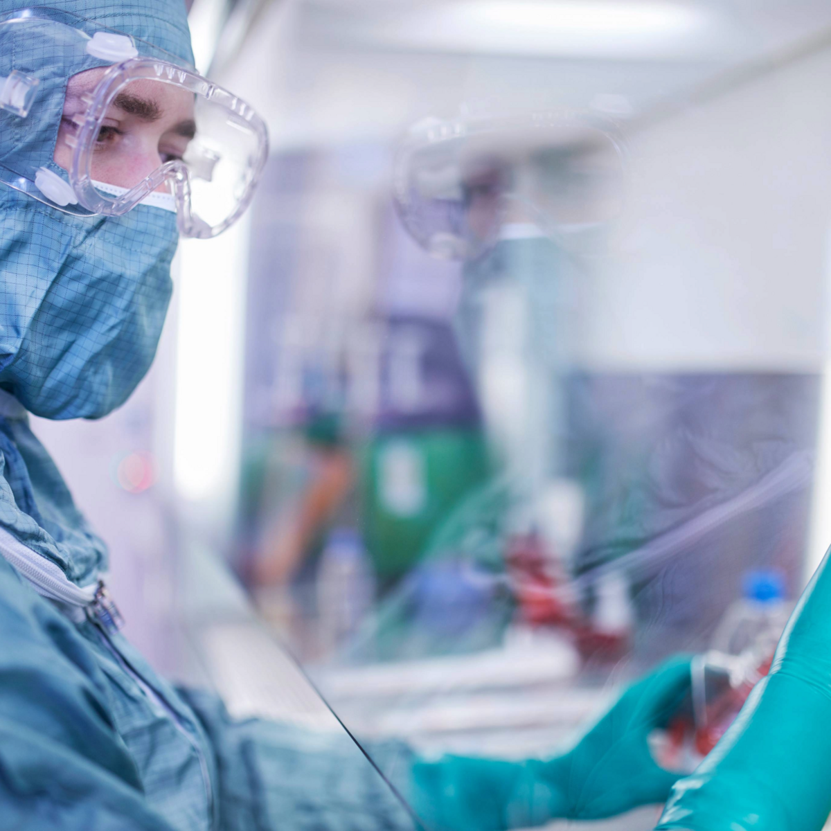 The picture shows a section of a laboratory worker in a clean room suit working on a sample from the right side.