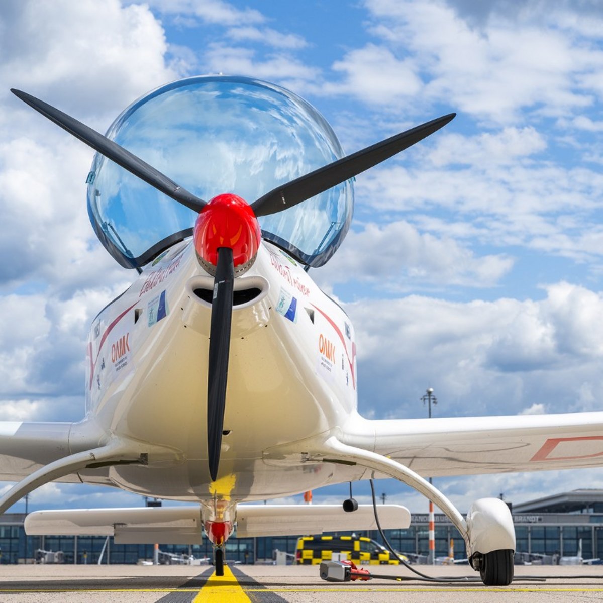 View from below of the all-electric “Elektra Trainer”: The propeller and the front section of the aircraft are shown from the front, with the fuselage and wings silhouetted against the sky above.