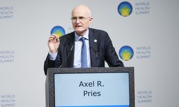 The picture shows an older man with glasses standing at a lectern and giving a speech. His name is written on the lectern: Axel. R. Pries