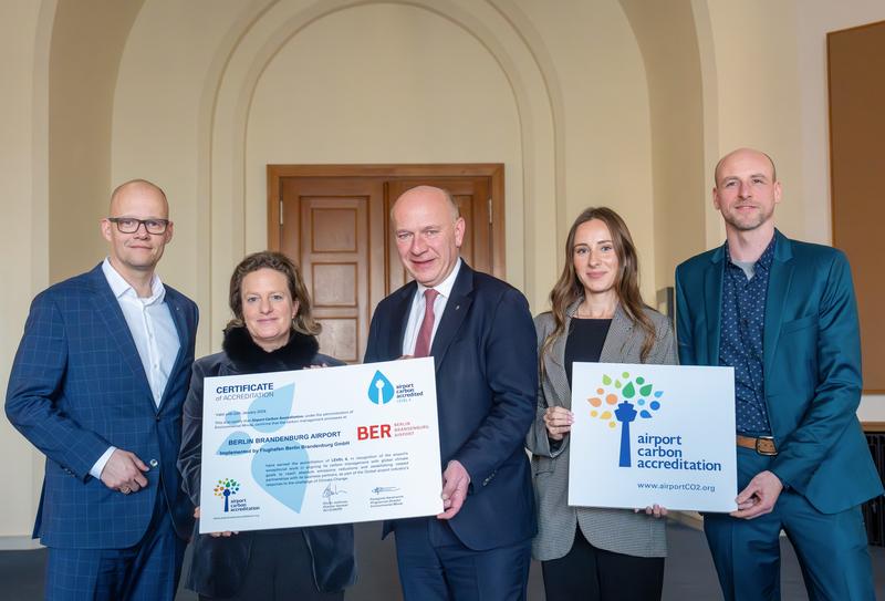 The following individuals are holding signs displaying the award for CO₂ management under the Airport Carbon Accreditation: Level 4 of the Airport Carbon Accreditation: Dr. Arne Diedrich, Sustainability Manager at FBB; Aletta von Massenbach, Chair of the Management Board of FBB; Kai Wegner, Governing Mayor of Berlin; Anna Panckow, Sustainability Communications Expert at FBB; Anton Förtsch, Sustainability Manager at FBB.