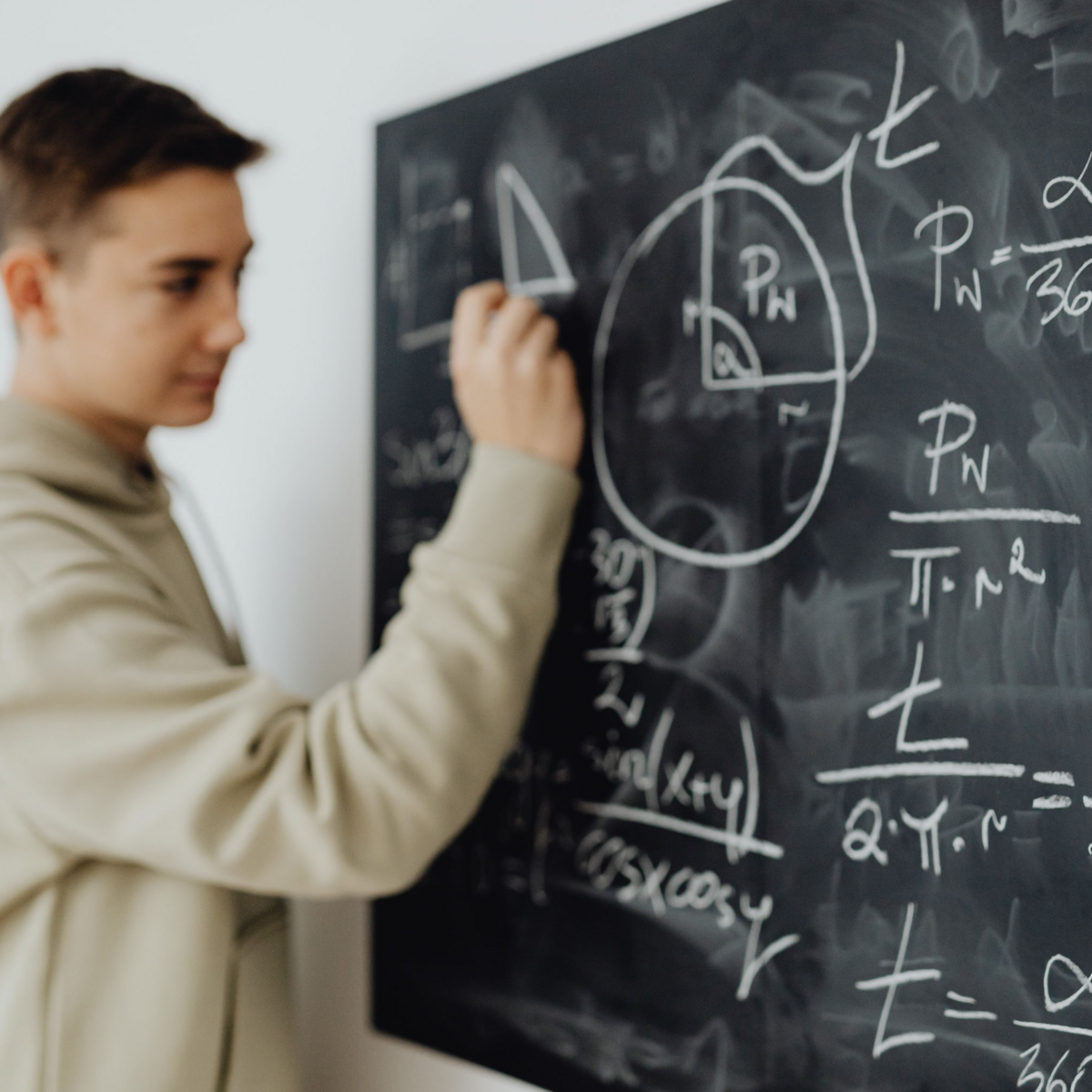 Image shows a teenager solving complex math problems on a blackboard