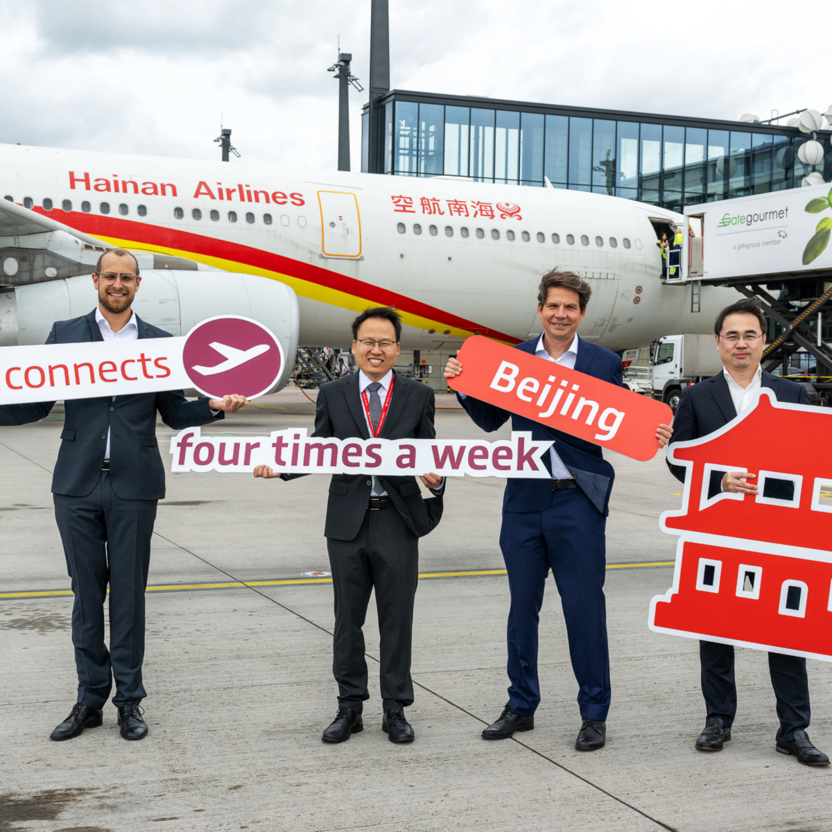  Picture shows 4 men in front of a Hainan Airlines plane for the ceremonial announcement of the expansion of flight connections to four times a week. The men are holding signs in front of them to make this clear.