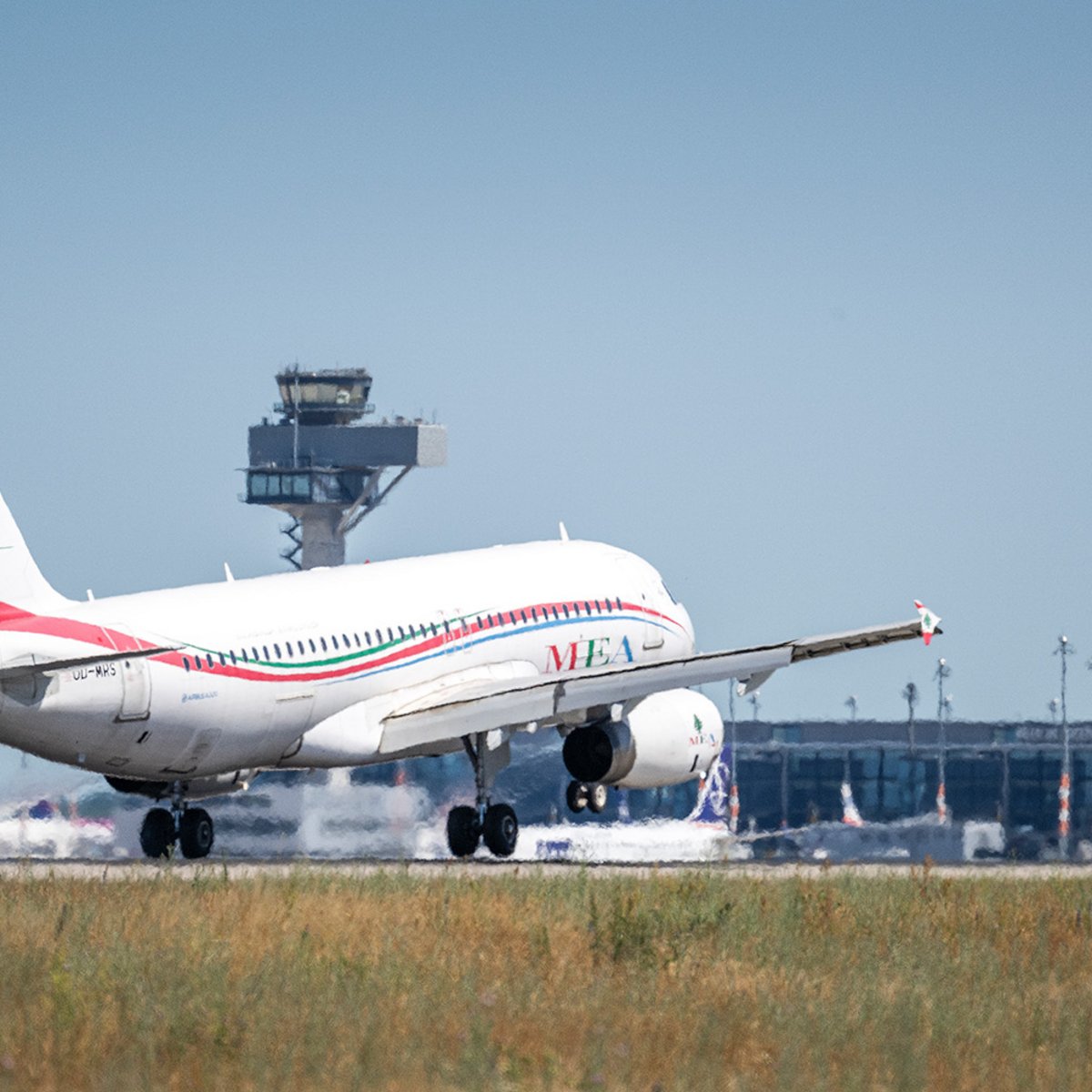 A Middle East Airlines aircraft on its final approach to Berlin Brandenburg Airport (BER), with the control tower and Terminal 1 in the background.