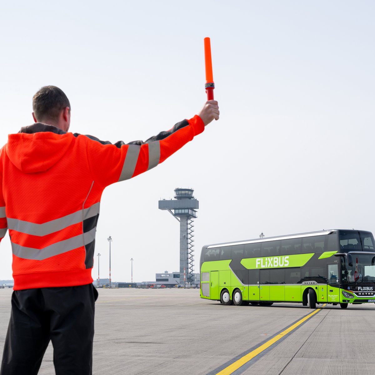An air traffic controller symbolically points the way to a FlixBus in front of the control tower at Berlin Brandenburg Airport (BER).