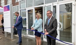 The picture shows a woman and two men people ceremoniously cutting a ribbon to open a new company location.